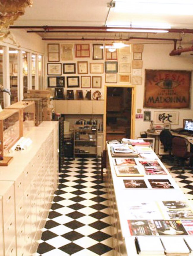 Interior of a colorful puppet museum with display cases, various puppets hanging from the ceiling, and framed pictures on the walls.