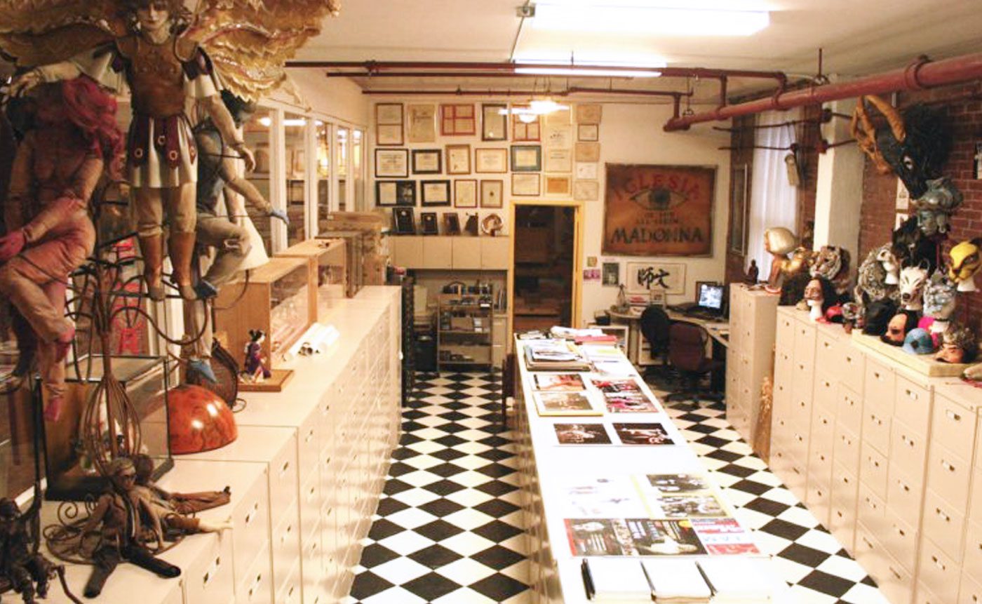 Interior of a colorful puppet museum with display cases, various puppets hanging from the ceiling, and framed pictures on the walls.