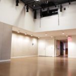 Modern empty hallway with beige walls, wooden flooring, white doors, and lighting fixtures mounted on the ceiling.