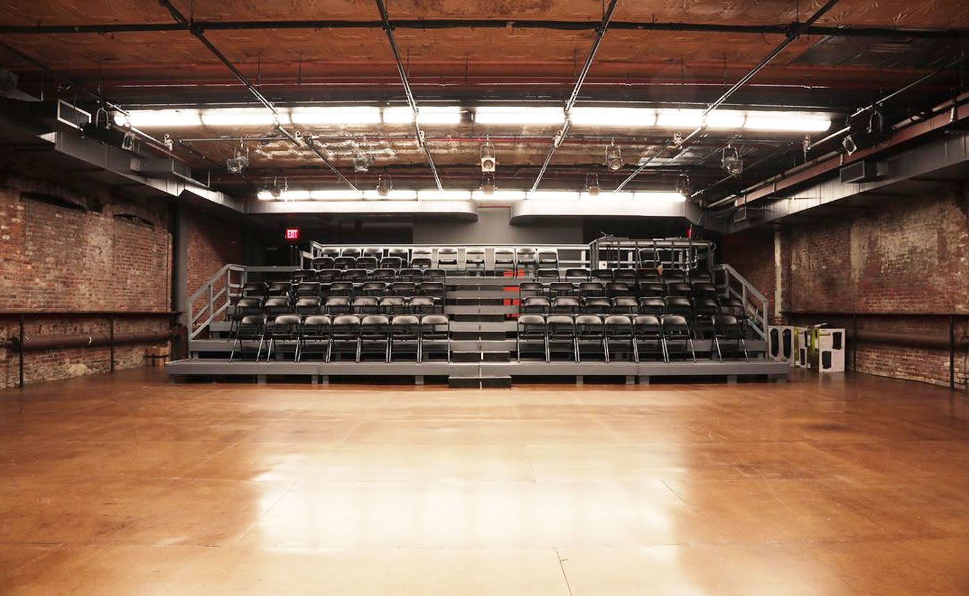 Empty theater stage with black chairs.