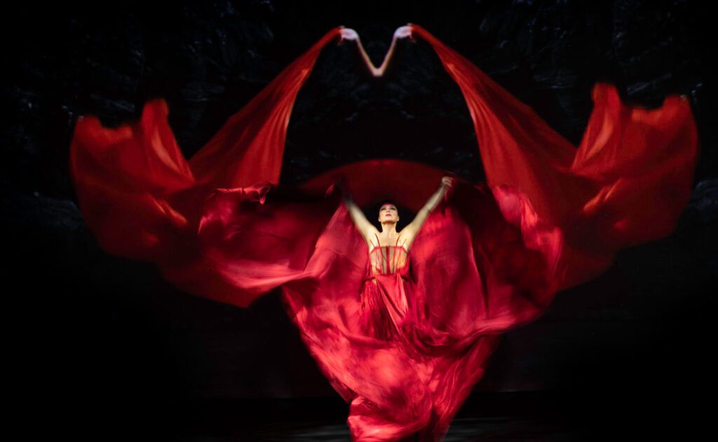 A woman in a red dress is dancing on a dark stage.