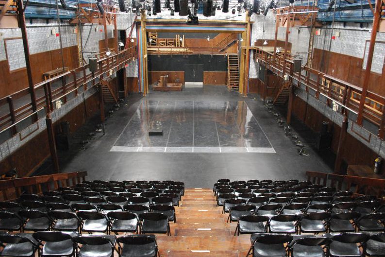 A large auditorium with rows of black chairs.