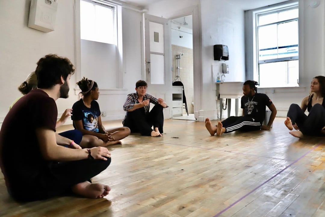 A group of people sitting on the floor in an empty room.