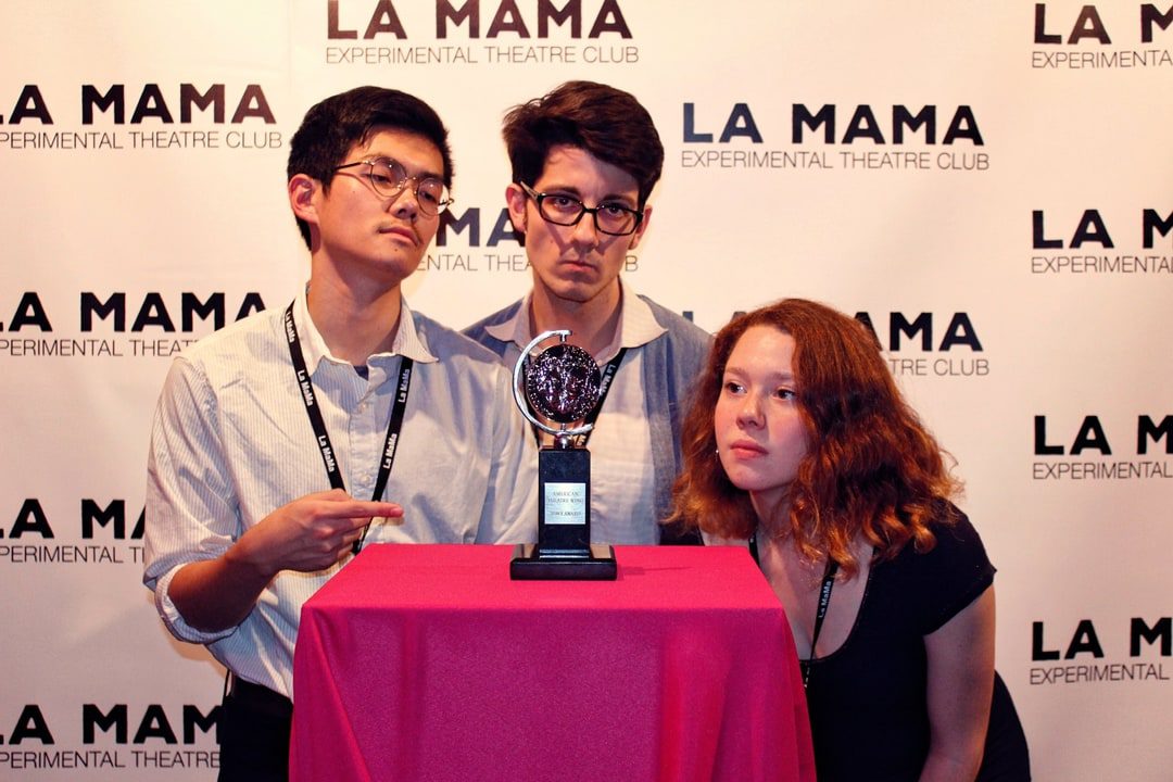 Three people posing in front of a table with a la mama award.