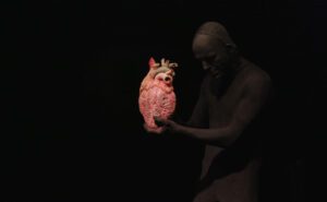 A man holding a heart in front of a black background.