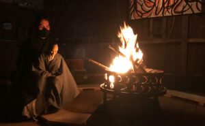 A man sitting in front of a fire with a mask on.