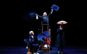 A group of people standing on a stage with blue umbrellas.