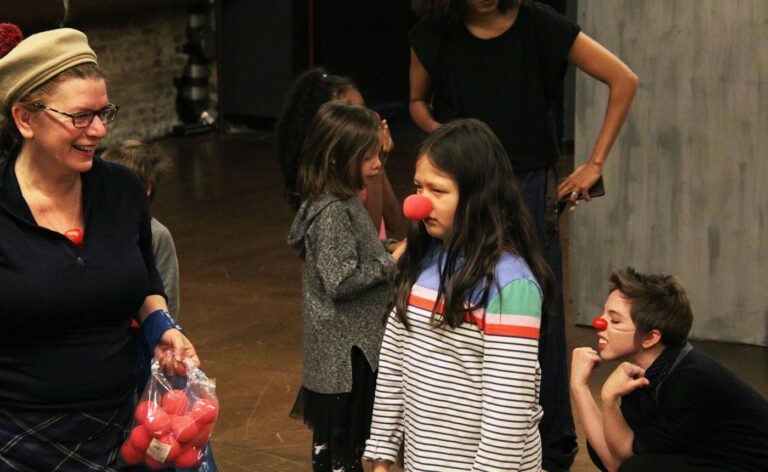 A woman with a clown nose standing next to a group of children.