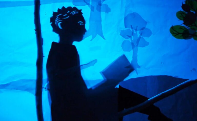 A silhouette of a man reading a book under a blue light.