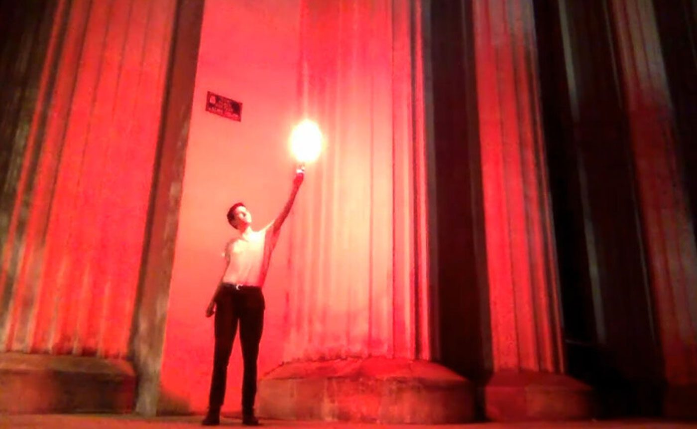 A man holding a torch in front of columns.