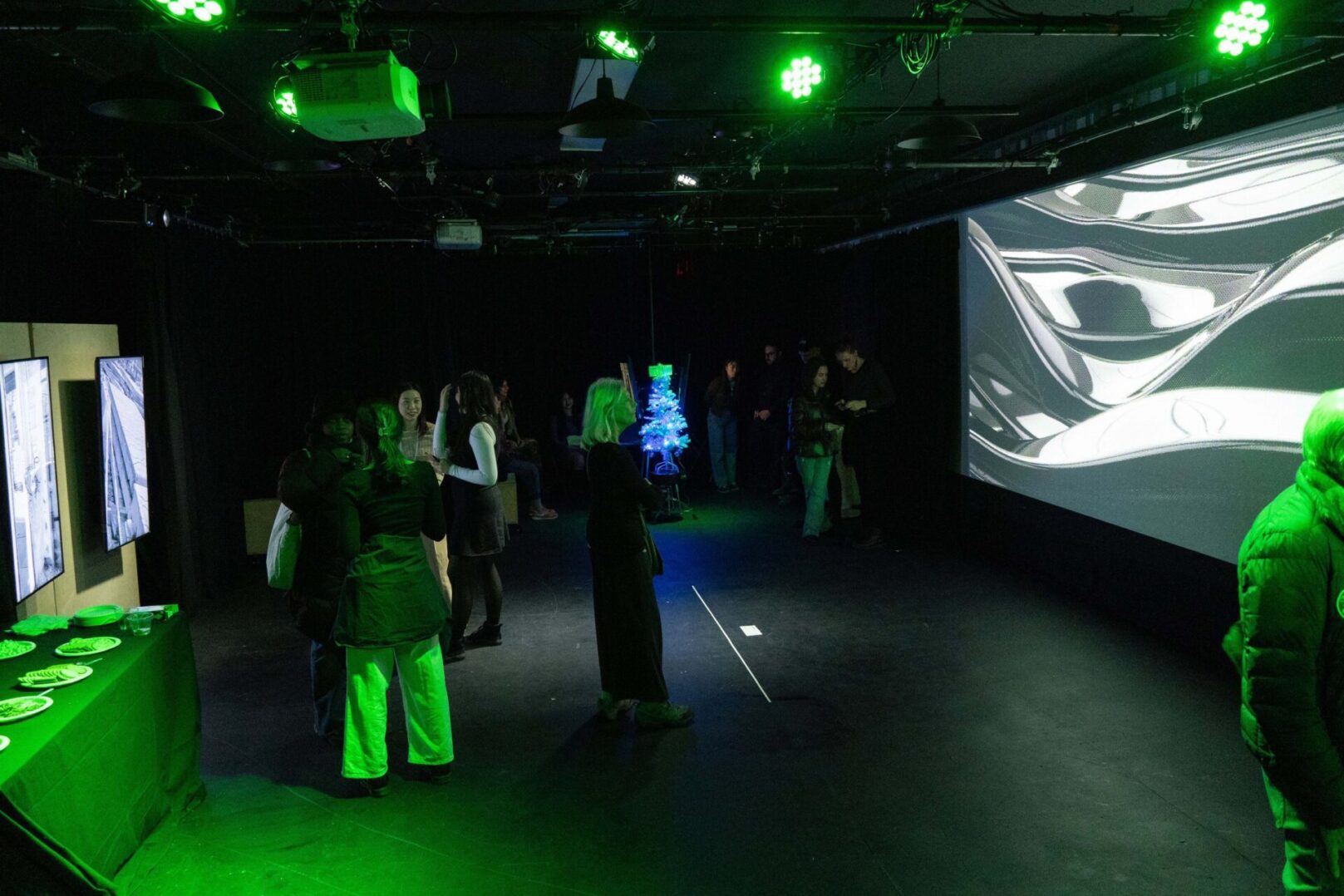 People viewing digital artwork in a dimly lit gallery with green lighting and projected images on the wall.