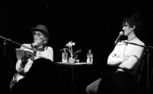 Two people sitting at a table with microphones in front of them.