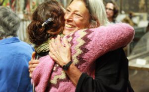 A woman is hugging another woman in an art gallery.