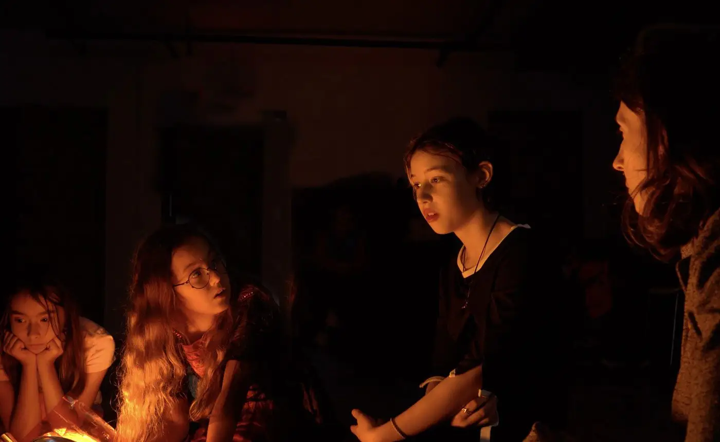 Group of teenagers gathered around a warm glow, sharing stories in a dimly lit room.