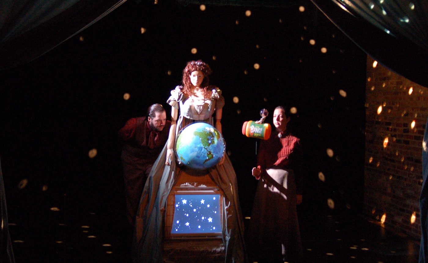 A woman holds a globe on stage.